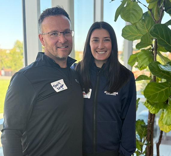A woman in graduation cap and gown holds up her degree and smiles